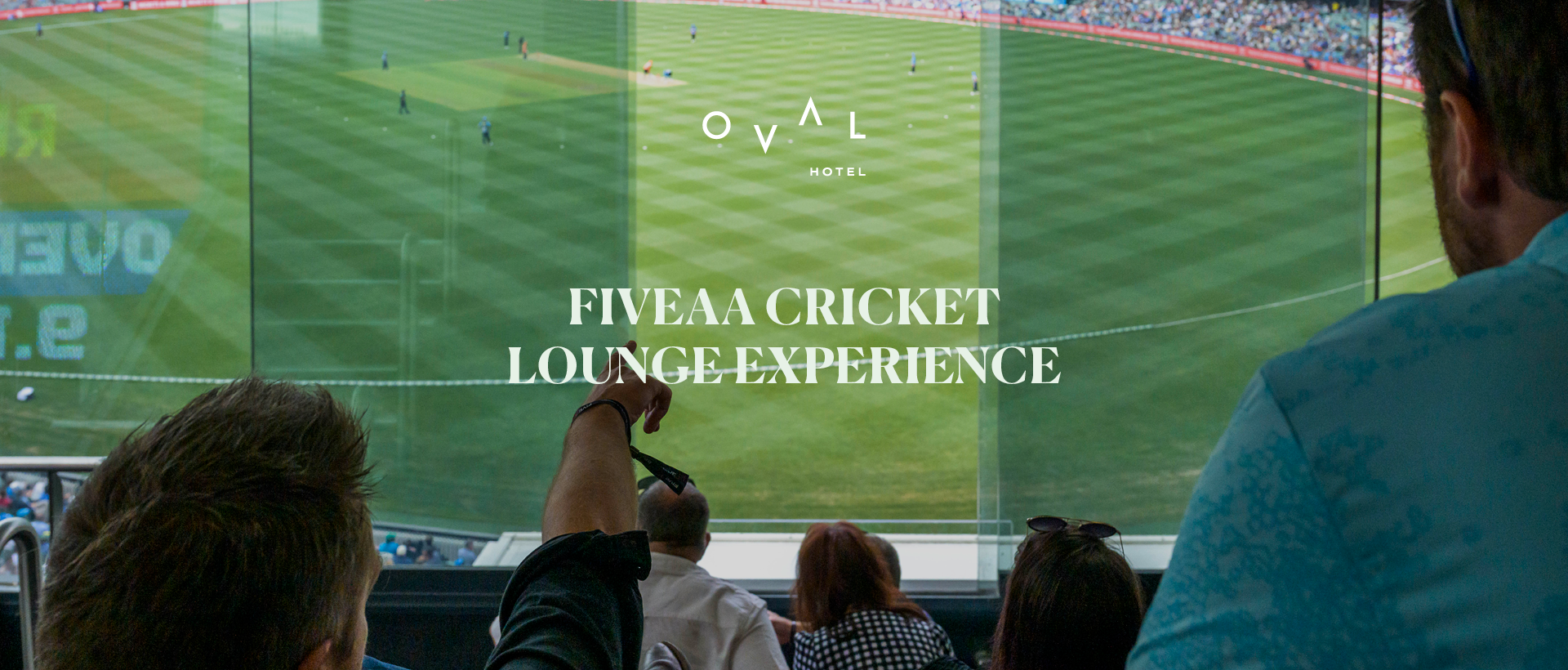 View of a cricket match from an elevated lounge, with spectators pointing towards the field and enjoying the game.